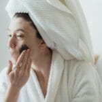 Kobieta w ręczniku nakłada maseczkę na twarz podczas porannej pielęgnacji