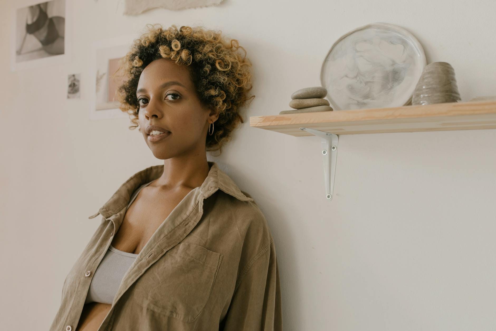 Kobieta z kręconymi farbowanymi włosami oparta o ścianę w jasnym wnętrzu