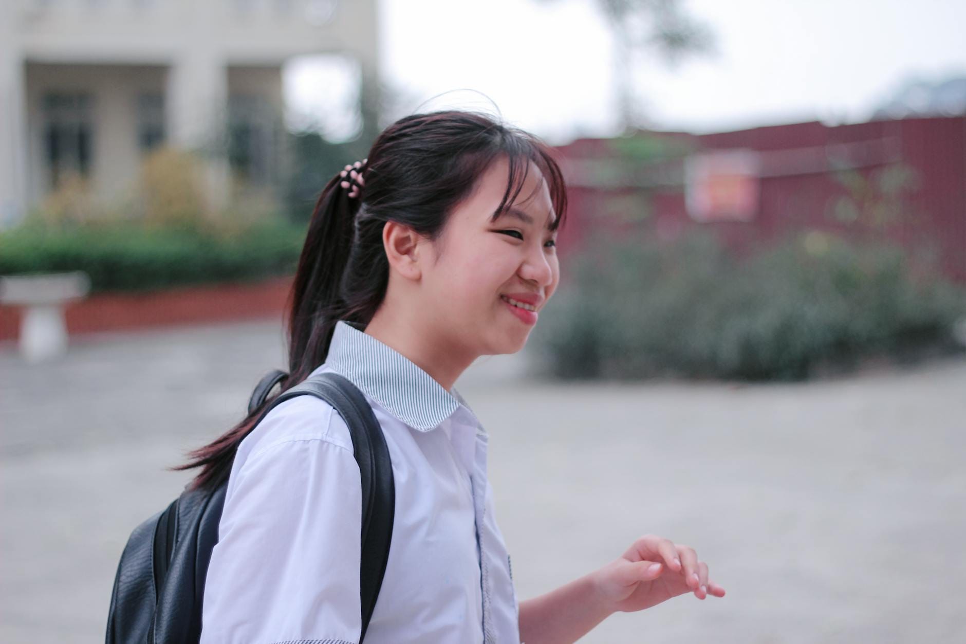 Uśmiechnięta uczennica w szkolnym mundurku z plecakiem na zewnątrz szkoły