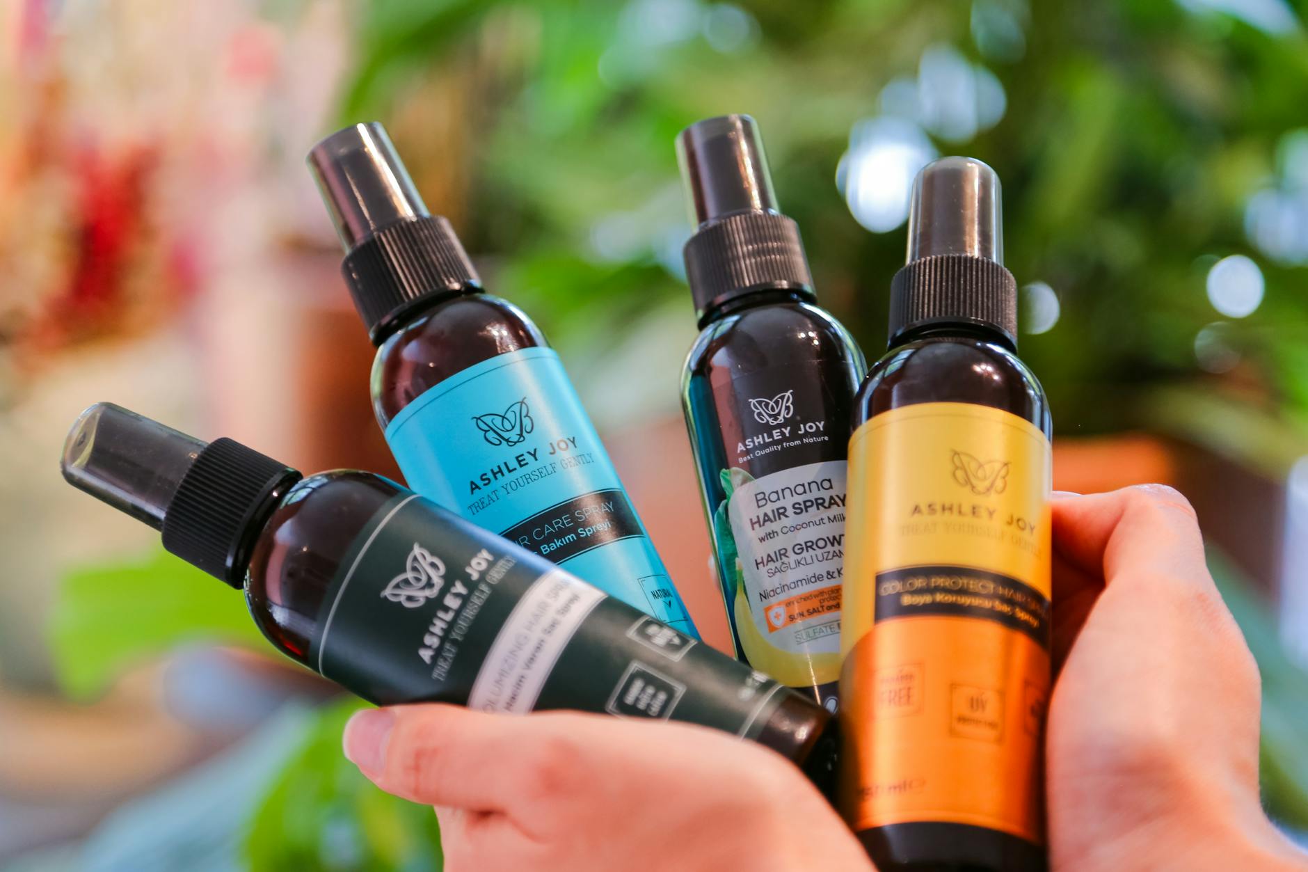 Dłonie trzymające butelki kosmetyków do pielęgnacji włosów Ashley Joy