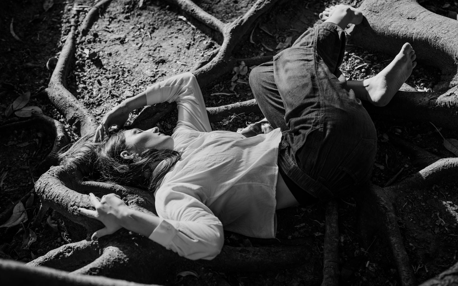 Kobieta z rozpuszczonymi włosami leży na korzeniach drzewa w czerni i bieli
