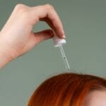 Dłoń nakłada serum pipetą na rude włosy z bliska