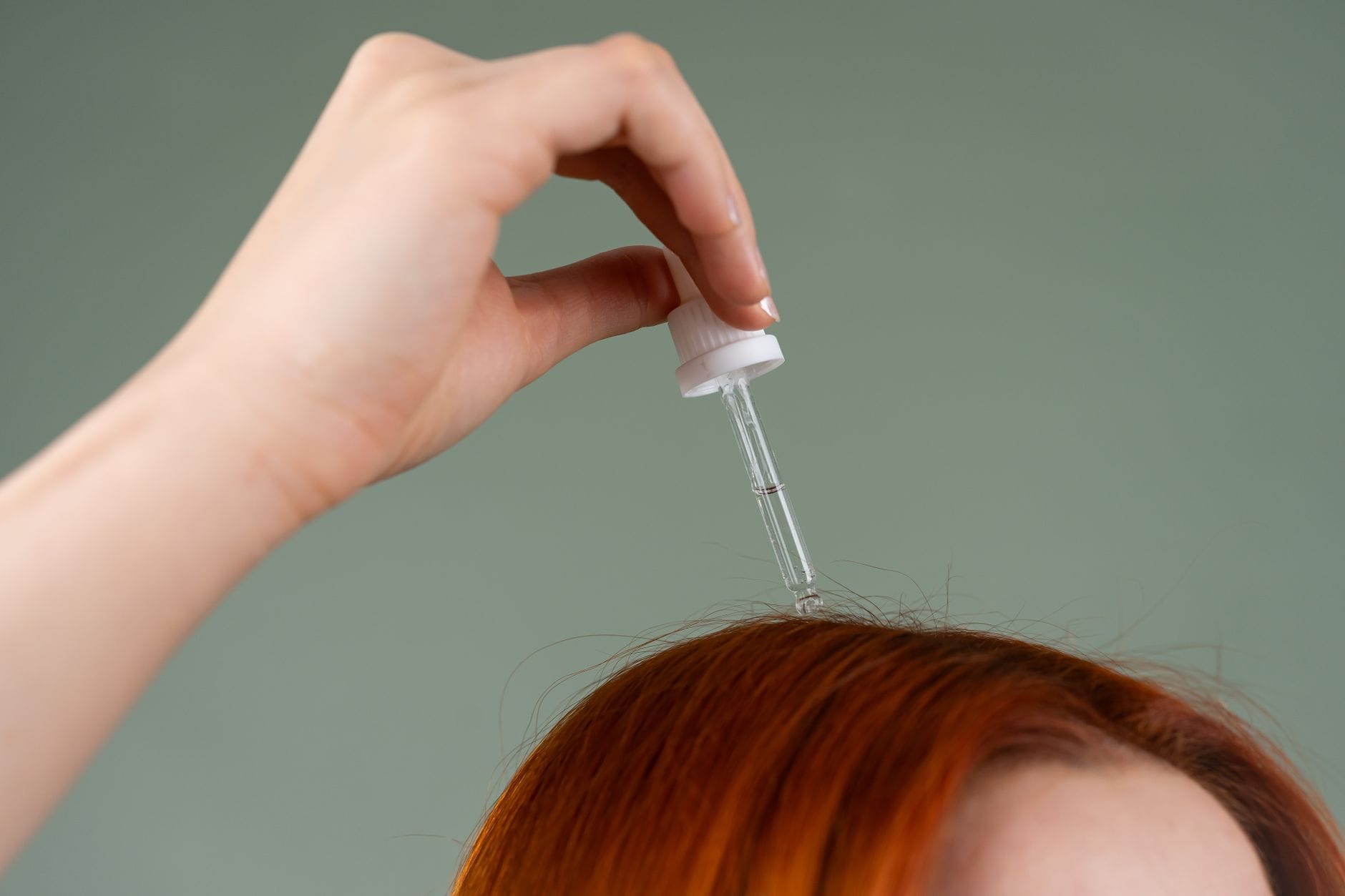 Dłoń nakłada serum pipetą na rude włosy z bliska